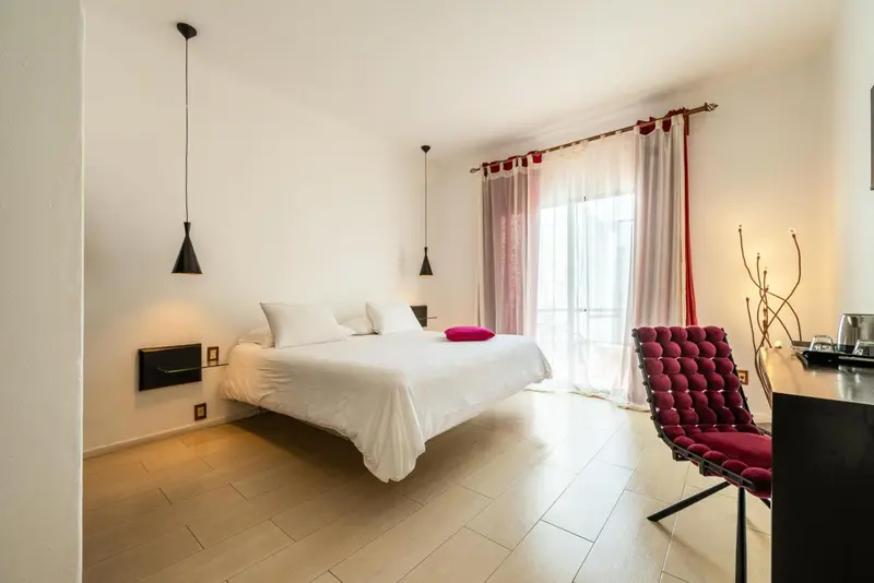 Une chambre lumineuse avec un grand lit et un fauteuil rouge.