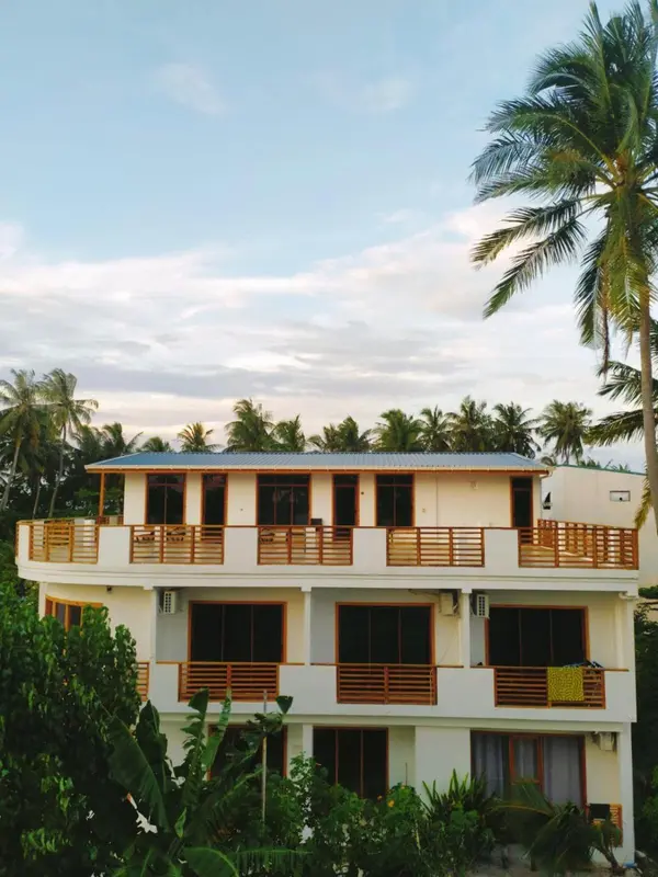 Bâtiment blanc à deux étages avec des balcons et une végétation luxuriante.