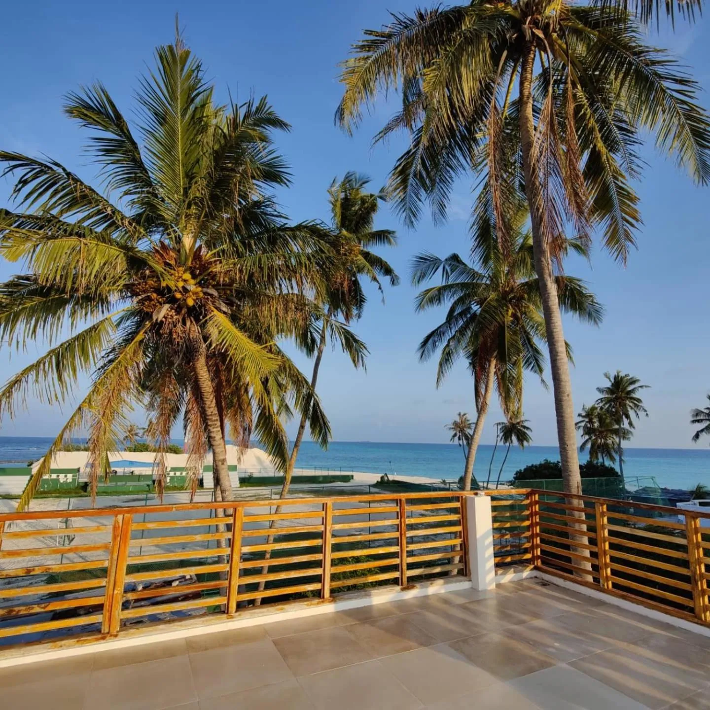 Terrasse en bois avec vue sur la mer et les palmiers.