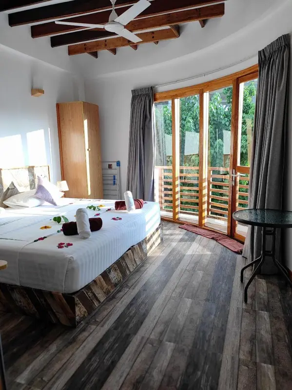 Une chambre lumineuse avec un lit décoré de fleurs et une terrasse accessible par de grandes baies vitrées.