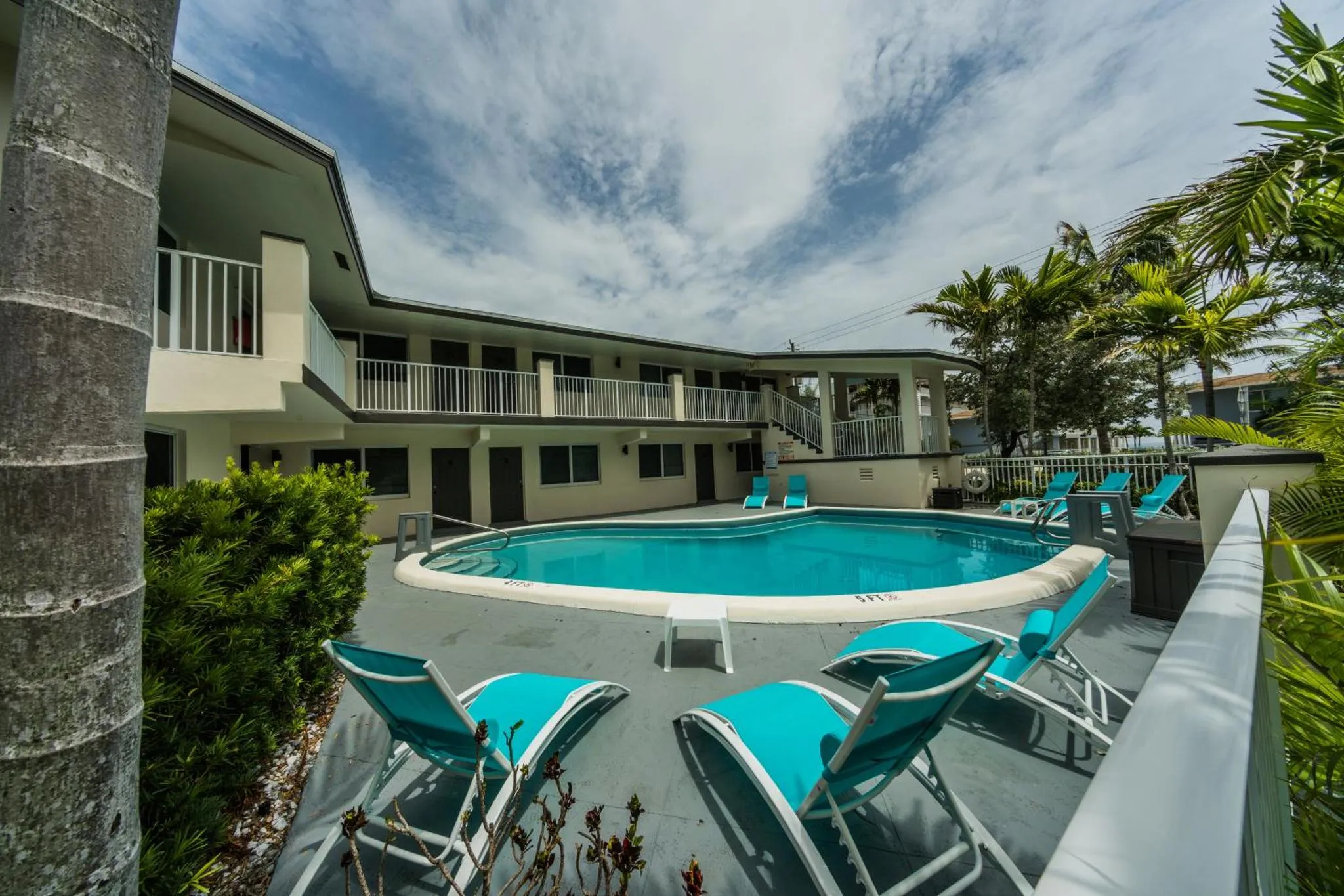 Transats bleus disposés autour d'une piscine rectangulaire dans un jardin tropical.