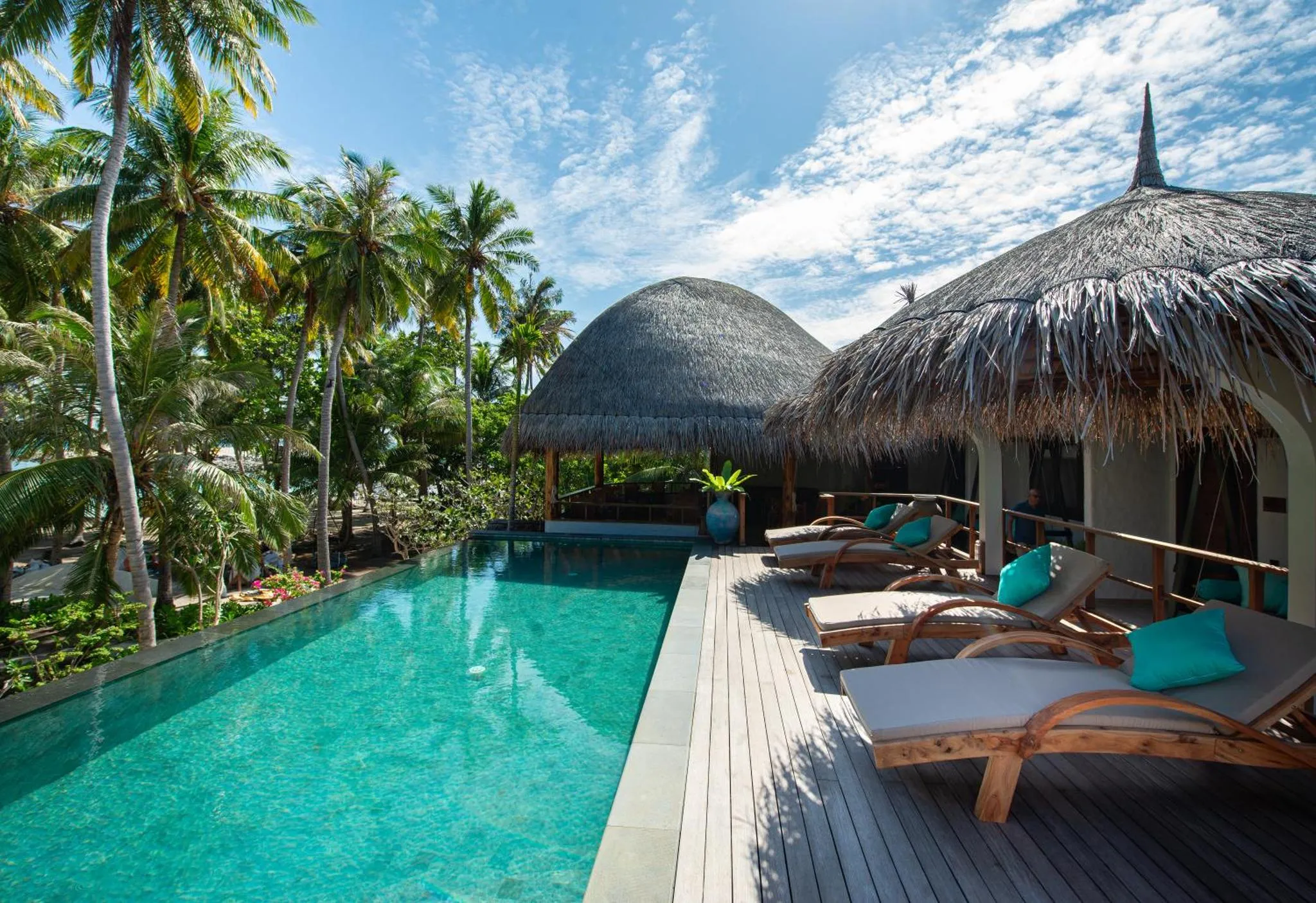 Terrasse avec transats et piscine turquoise bordée de végétation tropicale.