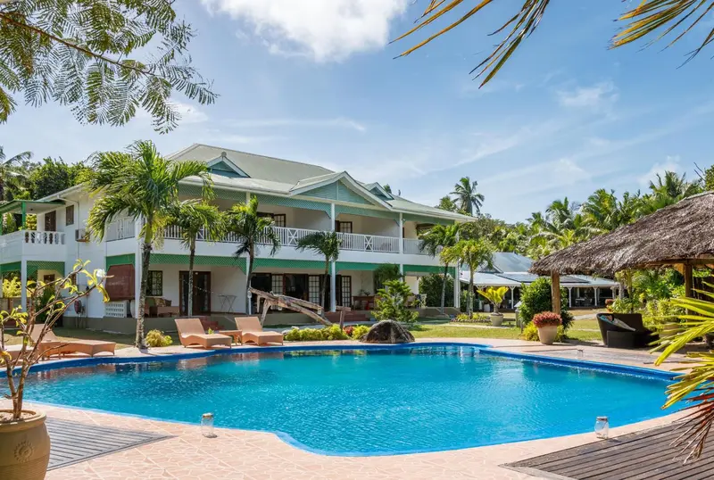 Bâtiment blanc avec des balcons et des palmiers, surplombant une piscine turquoise.
