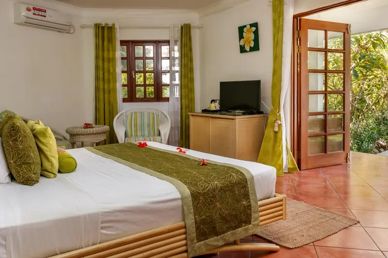 Une chambre lumineuse avec un lit décoré et une porte-fenêtre ouverte sur la végétation.