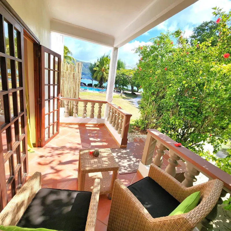 Terrasse ombragée avec mobilier en rotin donnant sur une plage et la mer.