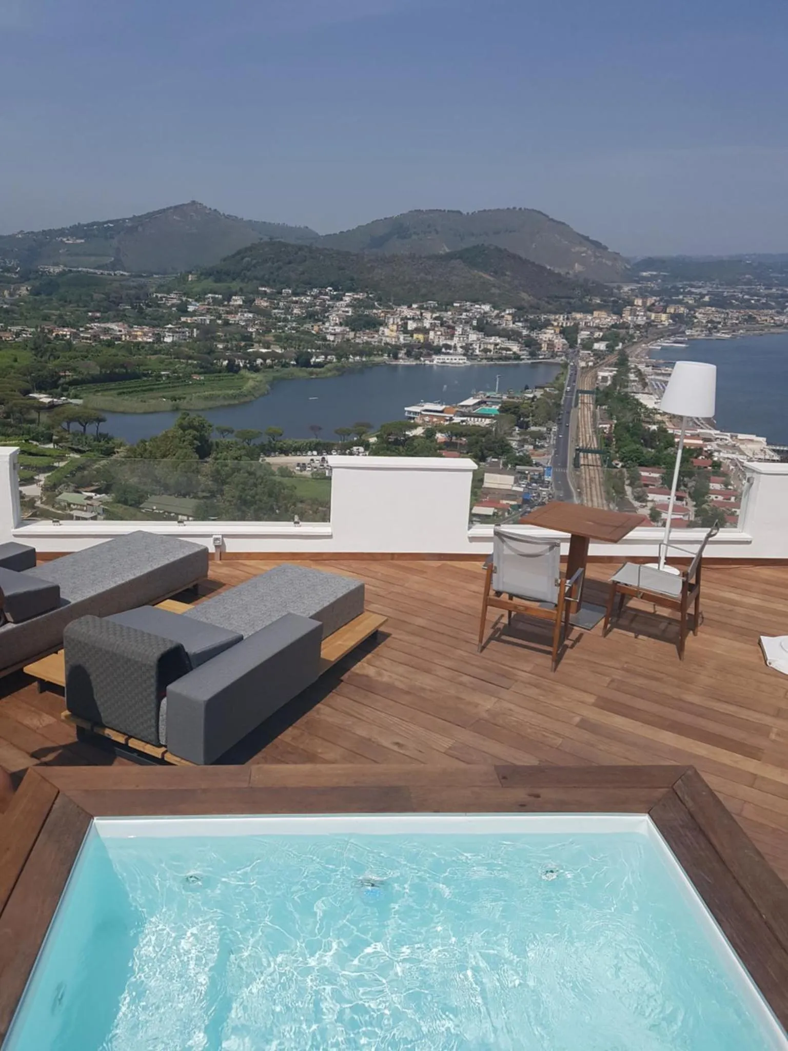 Terrasse avec mobilier de détente et petite piscine offrant une vue sur la mer et les collines.