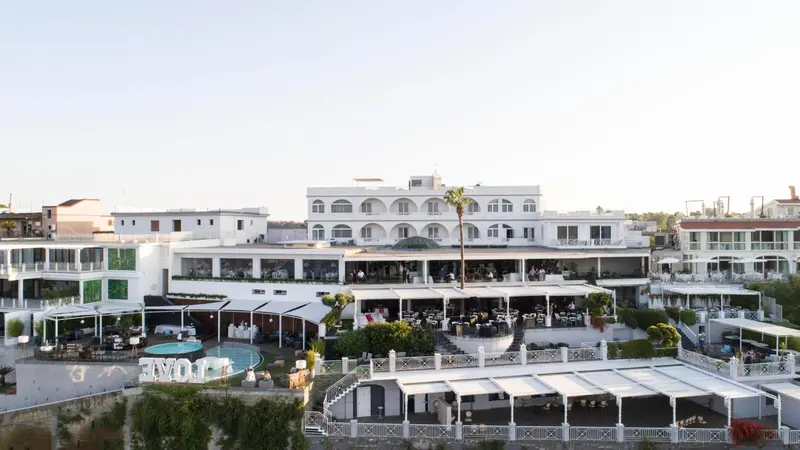 Bâtiment blanc à plusieurs niveaux avec des terrasses et une piscine en contrebas.