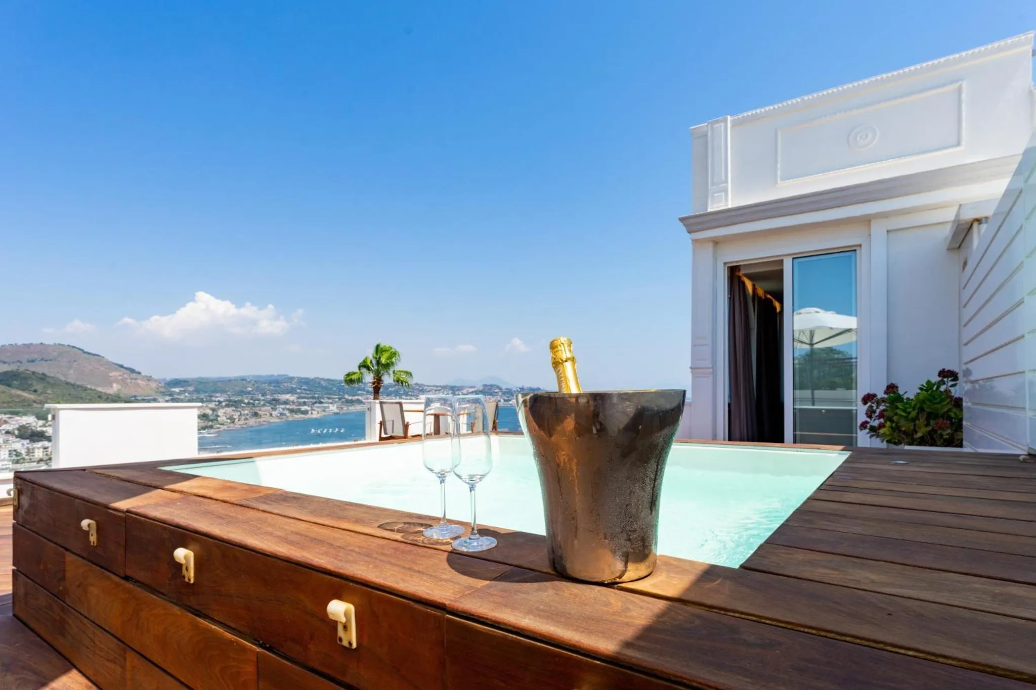 Une bouteille de champagne et deux verres sont posés sur le bord d'un jacuzzi avec vue sur la mer.