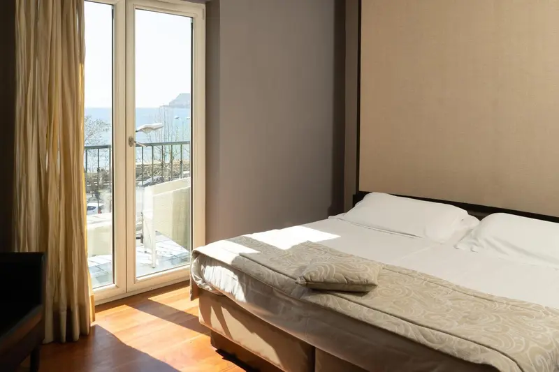 Une chambre lumineuse avec un lit et un balcon donnant sur la mer.