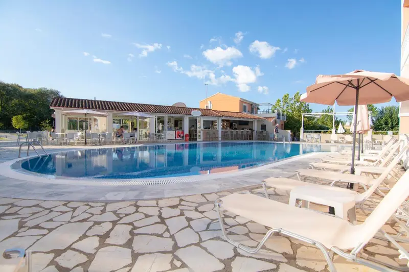 Transats blancs disposés autour d'une piscine bleue sous un parasol.