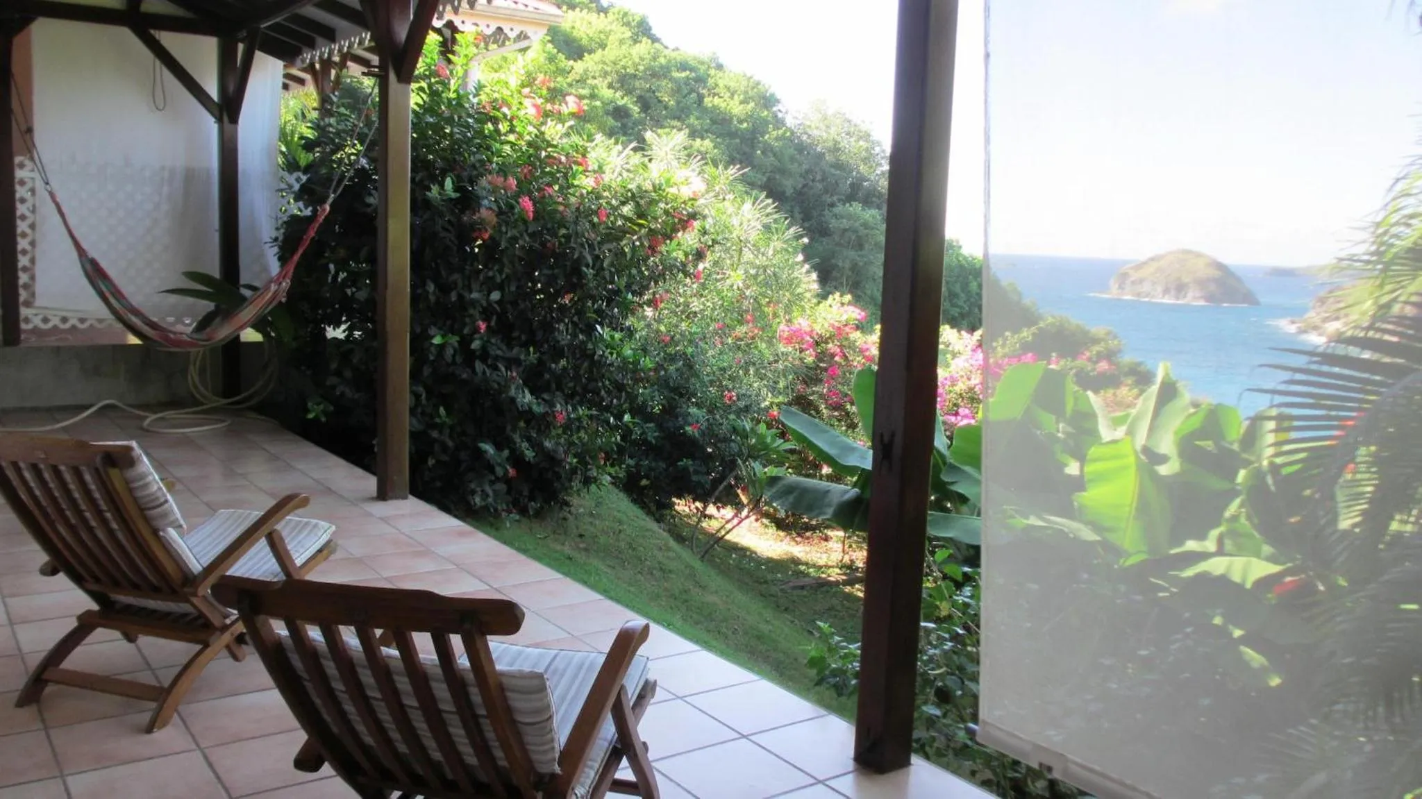 Deux fauteuils en bois invitent à la détente sur une terrasse ensoleillée avec vue sur la mer.