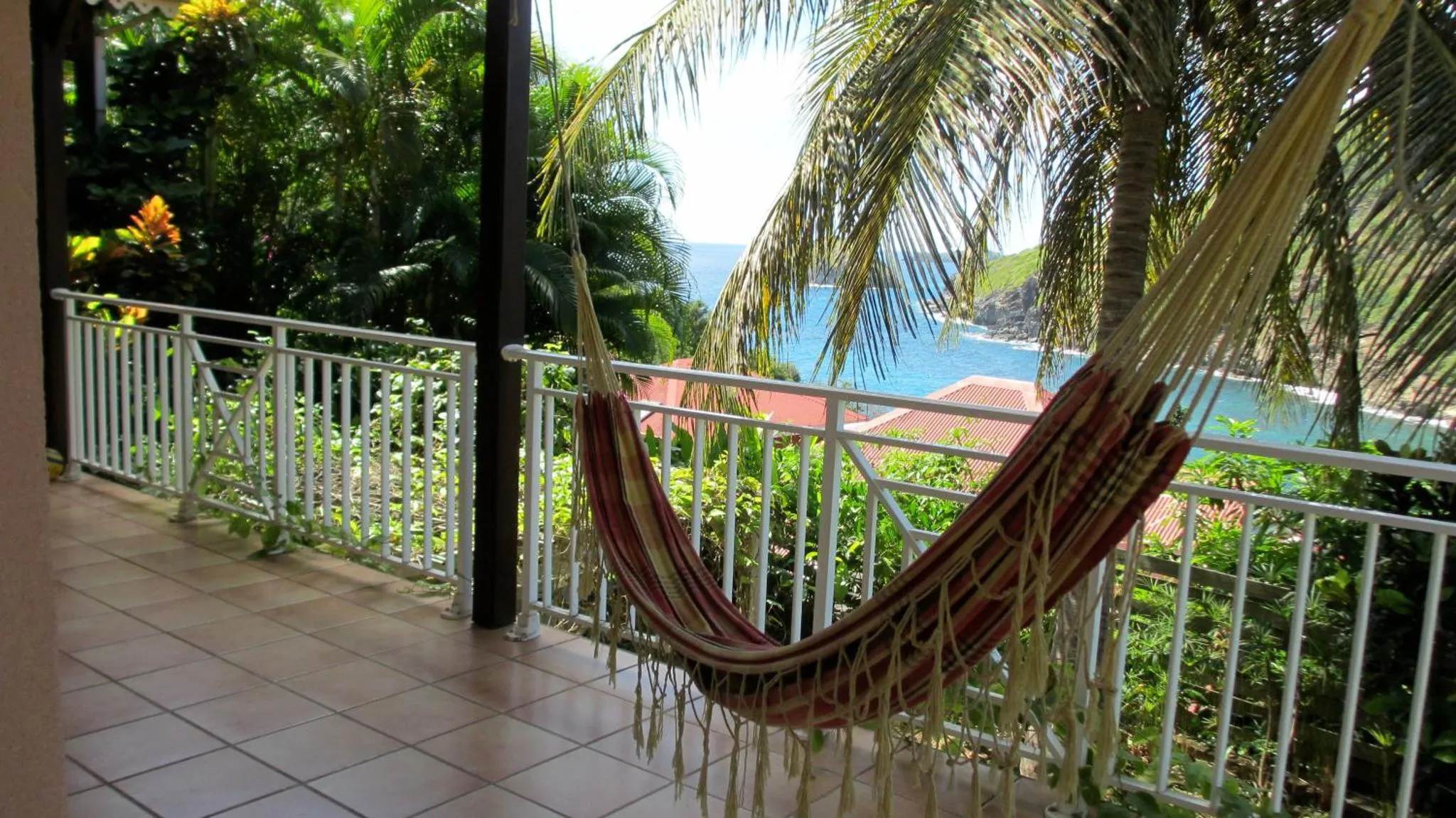Un hamac coloré est suspendu sur une terrasse carrelée avec vue sur la mer.