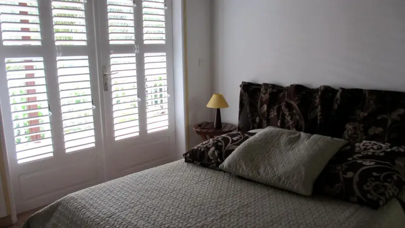 Une chambre lumineuse avec un lit recouvert d'une courtepointe et des volets blancs.