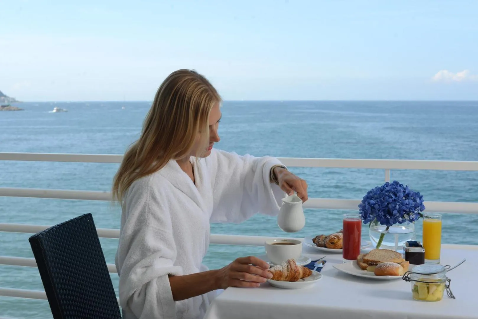 Une femme sert du café sur une terrasse avec vue sur la mer.