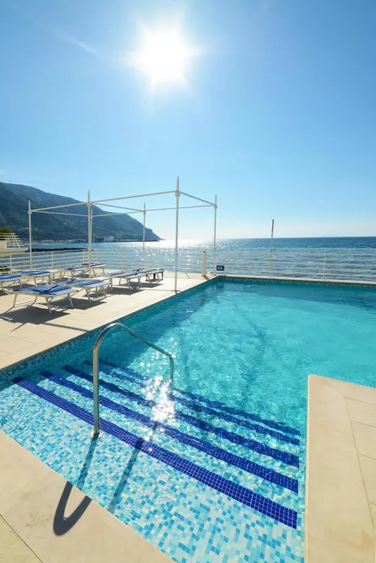 Une piscine bleue bordée de chaises longues ensoleillées surplombe la mer.