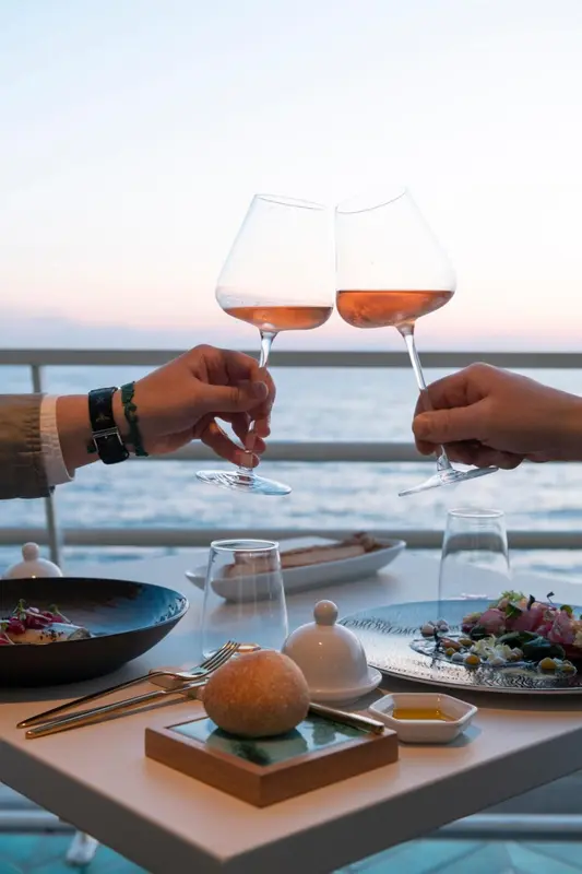 Deux verres de vin rosé sont portés à un toast sur une table dressée avec des plats.