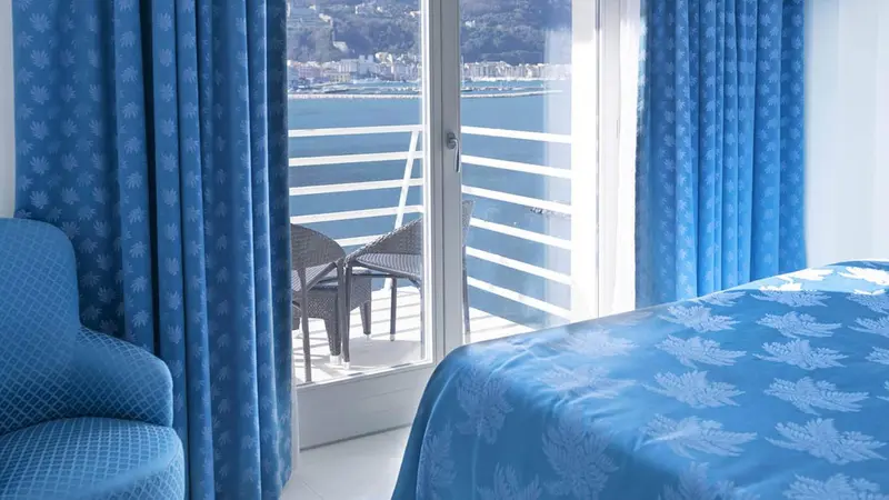 Une chambre lumineuse s'ouvre sur un balcon avec vue sur la mer.
