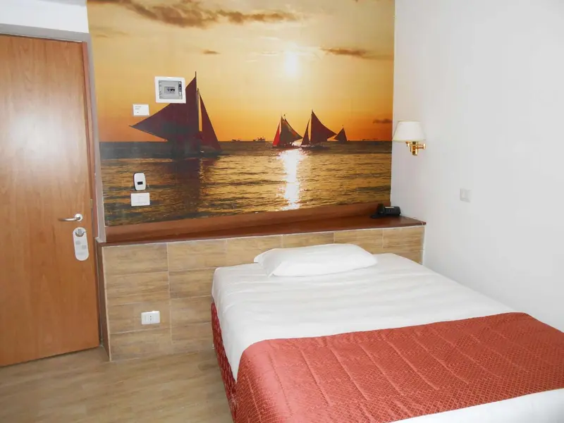 Une chambre avec un grand lit et un mur décoré d'une scène maritime au coucher du soleil.