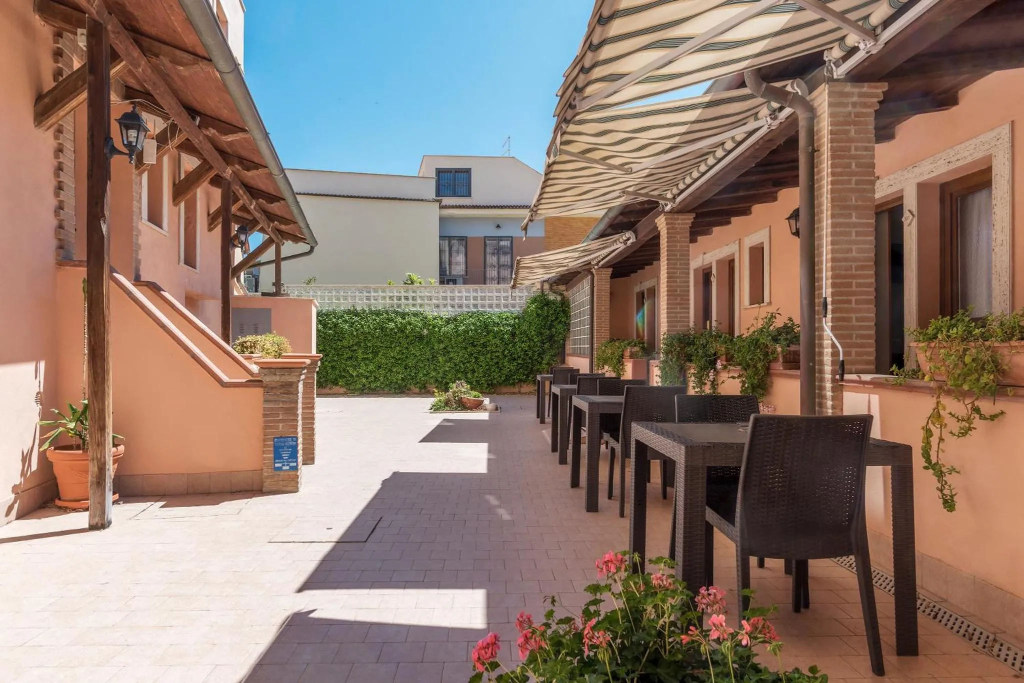 Terrasse ombragée avec tables et chaises devant un bâtiment aux murs pastel.