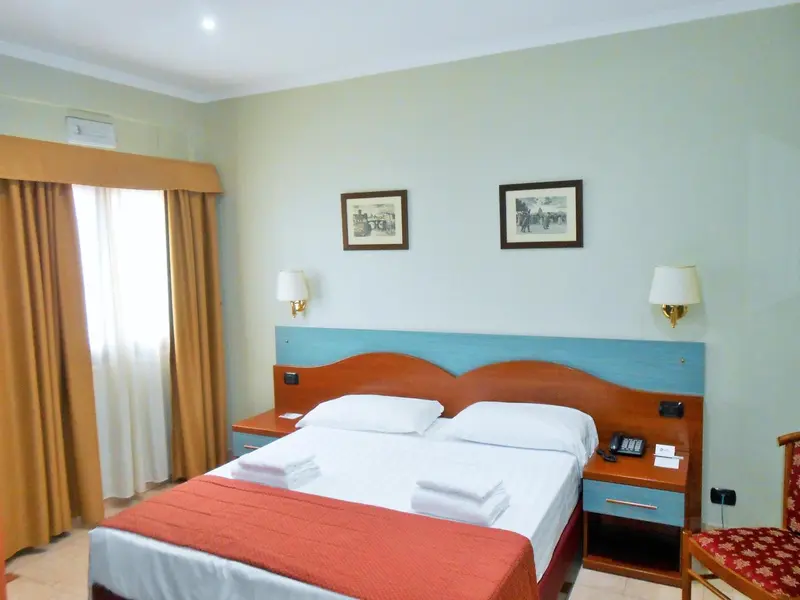 Une chambre lumineuse avec un grand lit et des rideaux orangés.