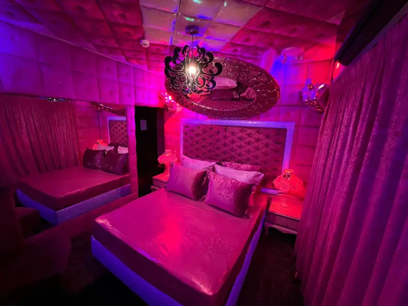Chambre à coucher avec lits décorés de tissus roses et d'éclairages colorés.