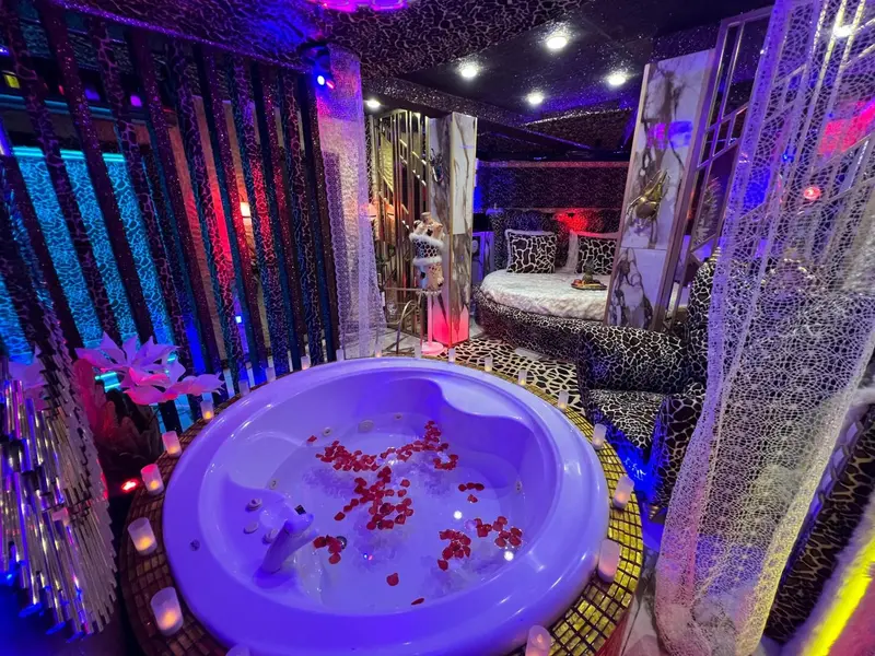 Un jacuzzi rempli d'eau et de pétales de fleurs rouges se trouve dans une chambre décorée de motifs animaliers et d'éclairages colorés.