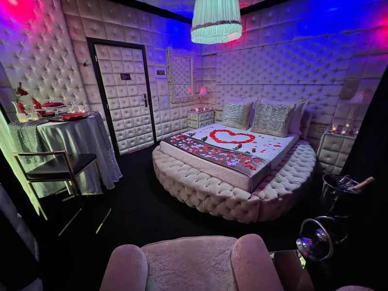 Une chambre décorée avec un lit rond recouvert de pétales de roses et une table avec un gâteau.