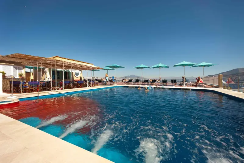 Une piscine rectangulaire avec une zone peu profonde et une zone plus profonde, entourée d'un sol carrelé et de parasols.