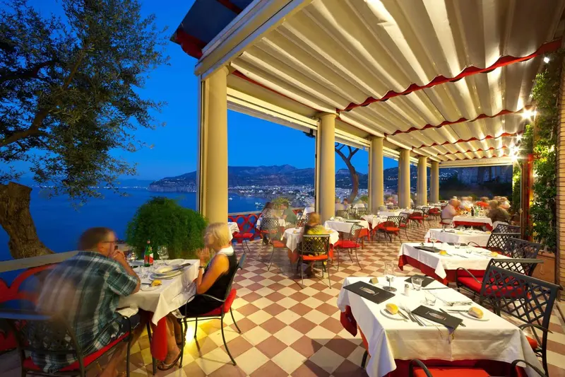 Une terrasse de restaurant offre une vue sur la mer et les lumières de la ville au crépuscule.