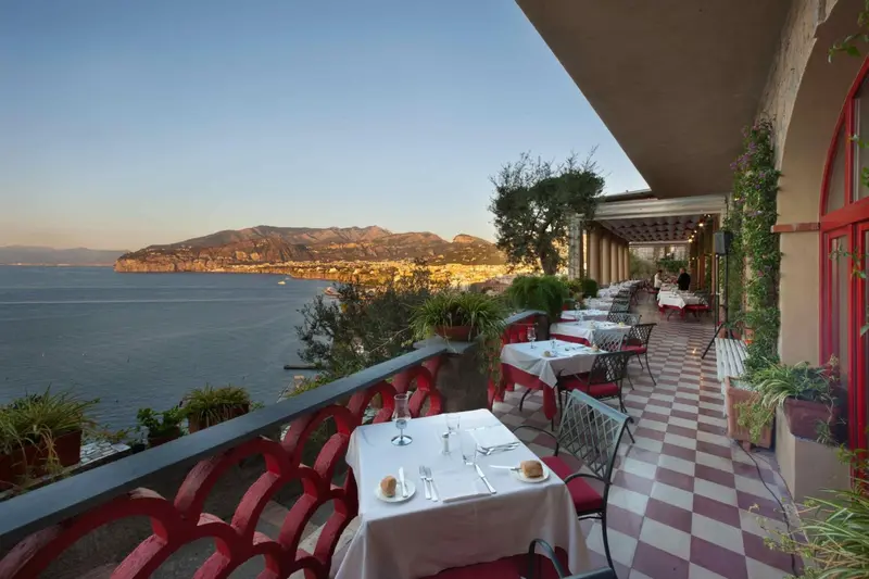 Terrasse de restaurant avec vue sur la mer et les montagnes au loin.