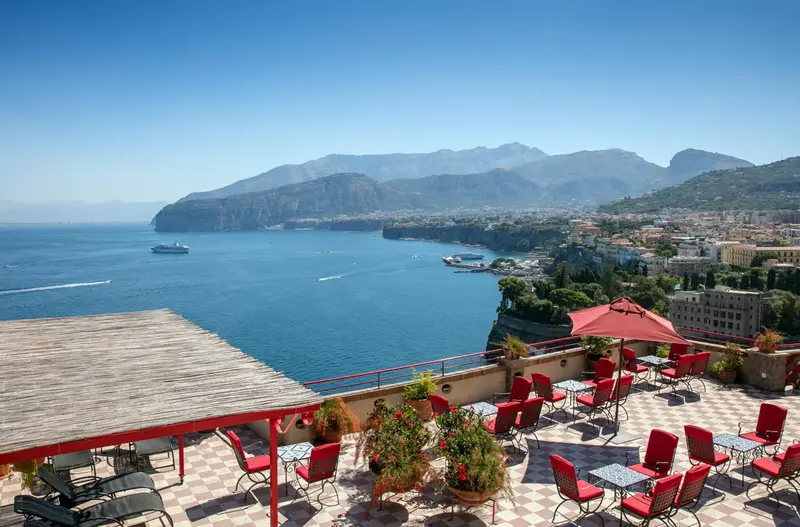 Terrasse avec mobilier rouge offrant une vue sur la mer et les montagnes.