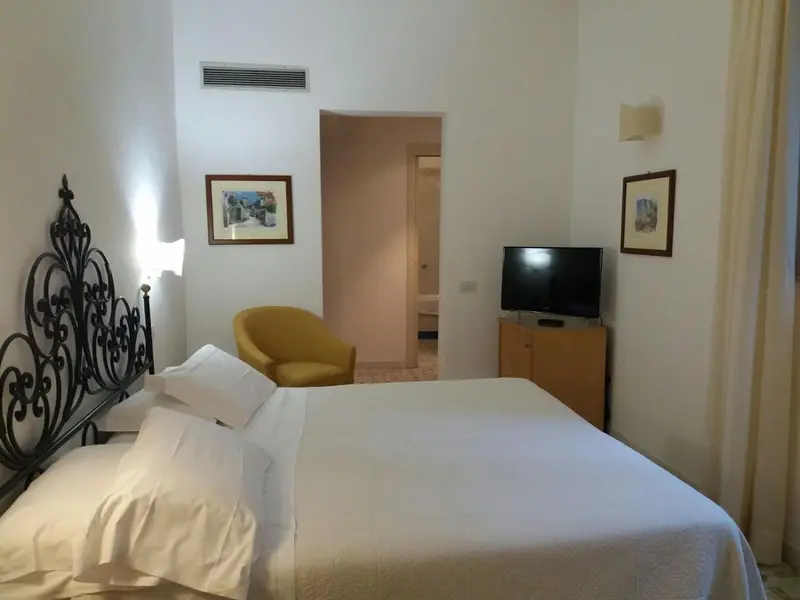 Une chambre lumineuse avec un lit recouvert d'une courtepointe blanche et une chaise jaune.