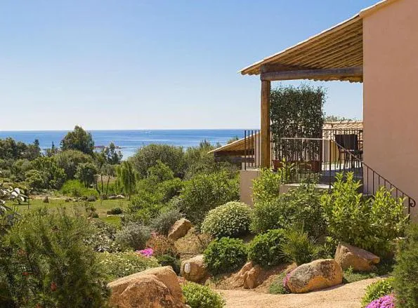 Vue d'une terrasse ombragée donnant sur la mer et la végétation.