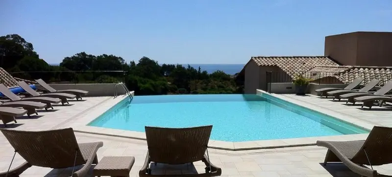 Transats et piscine au bord d'une terrasse ensoleillée avec vue sur la mer.