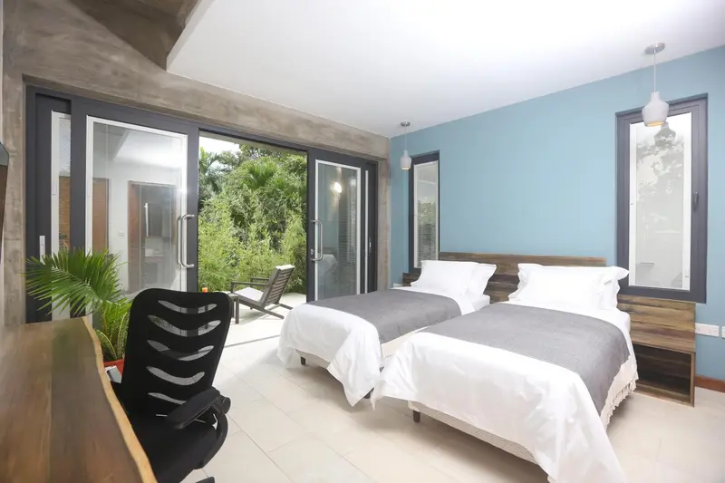Une chambre lumineuse avec deux lits simples et une vue sur la végétation.