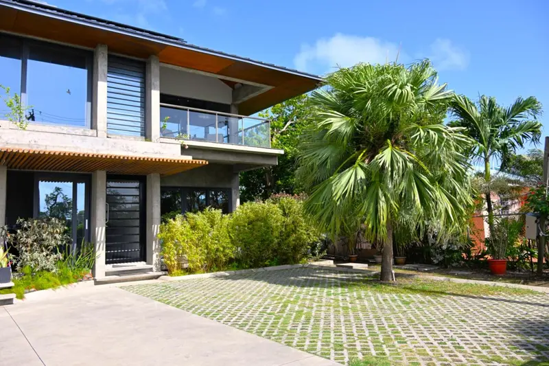 Bâtiment moderne avec balcon et végétation tropicale.