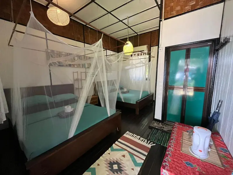 Une chambre avec deux lits recouverts de moustiquaires et une porte turquoise.