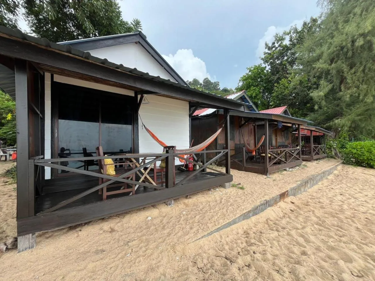 Rangée de bungalows en bois avec hamacs sur une terrasse face à une plage de sable.