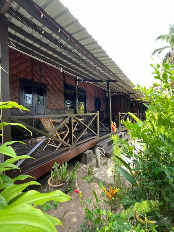 Terrasse en bois devant un bâtiment à l'architecture locale, entourée de végétation tropicale.
