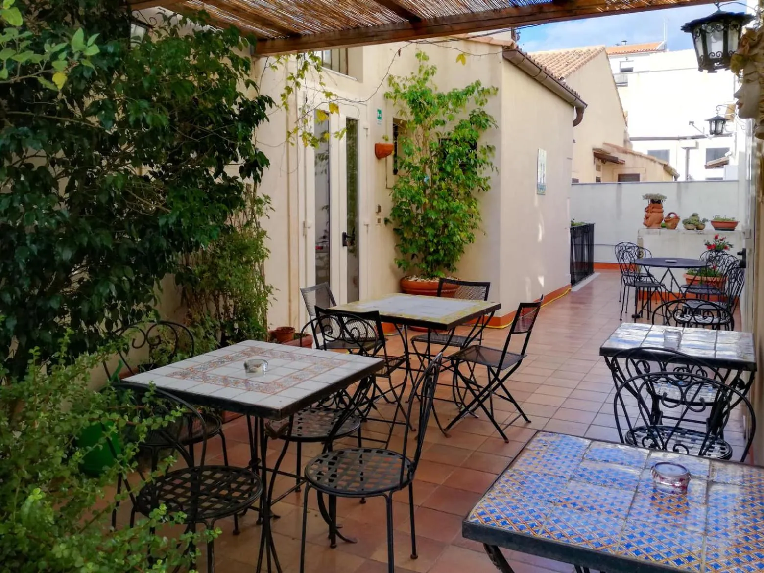 Terrasse ombragée avec tables et chaises en fer forgé.