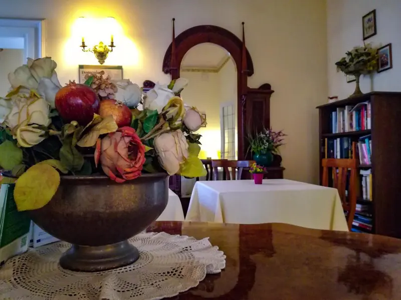 Une table en bois ornée d'un vase de fleurs et d'une nappe en dentelle se trouve dans une pièce lumineuse.