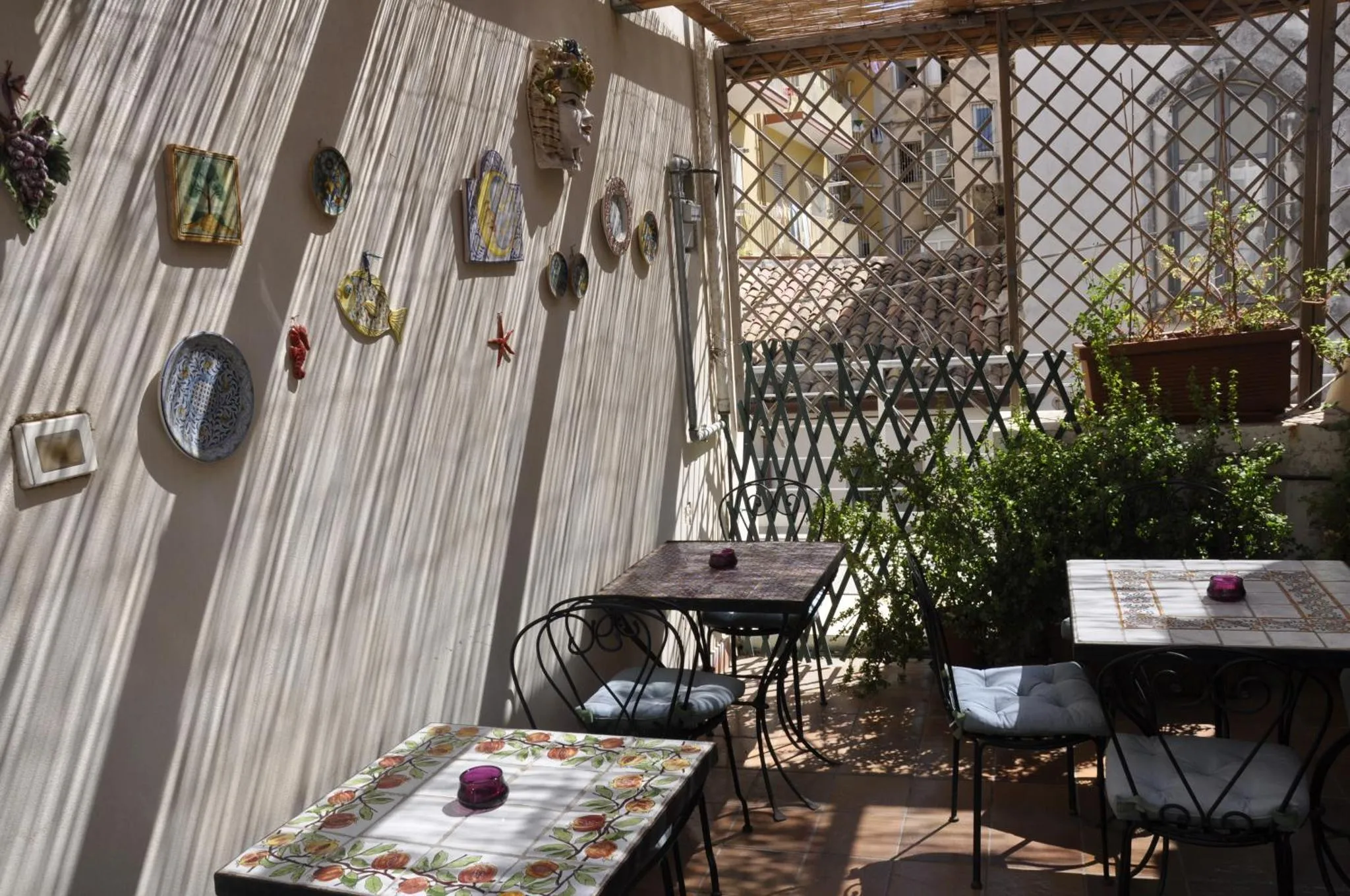 Terrasse ombragée avec tables et chaises décorées de céramiques murales.