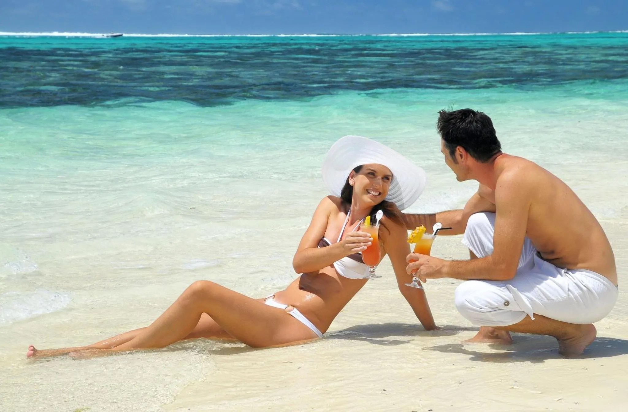 Un couple se détend sur une plage de sable blanc avec des cocktails.