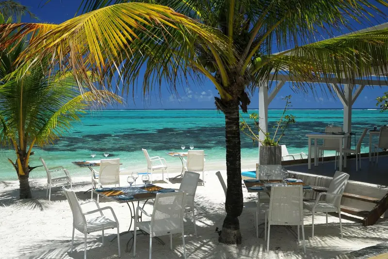Tables et chaises installées sur le sable blanc face à une mer turquoise.