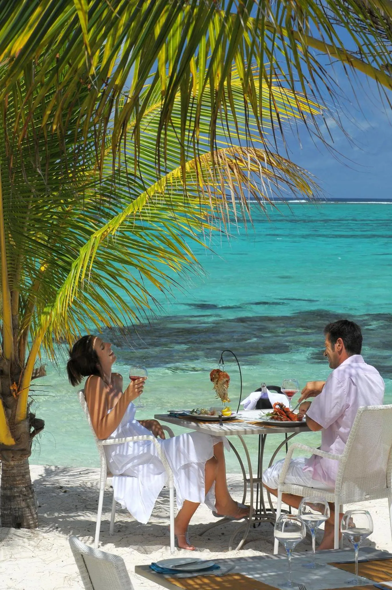 Un couple déguste des boissons sur une plage de sable blanc.