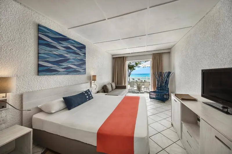 Une chambre lumineuse avec un grand lit et un canapé face à une baie vitrée.