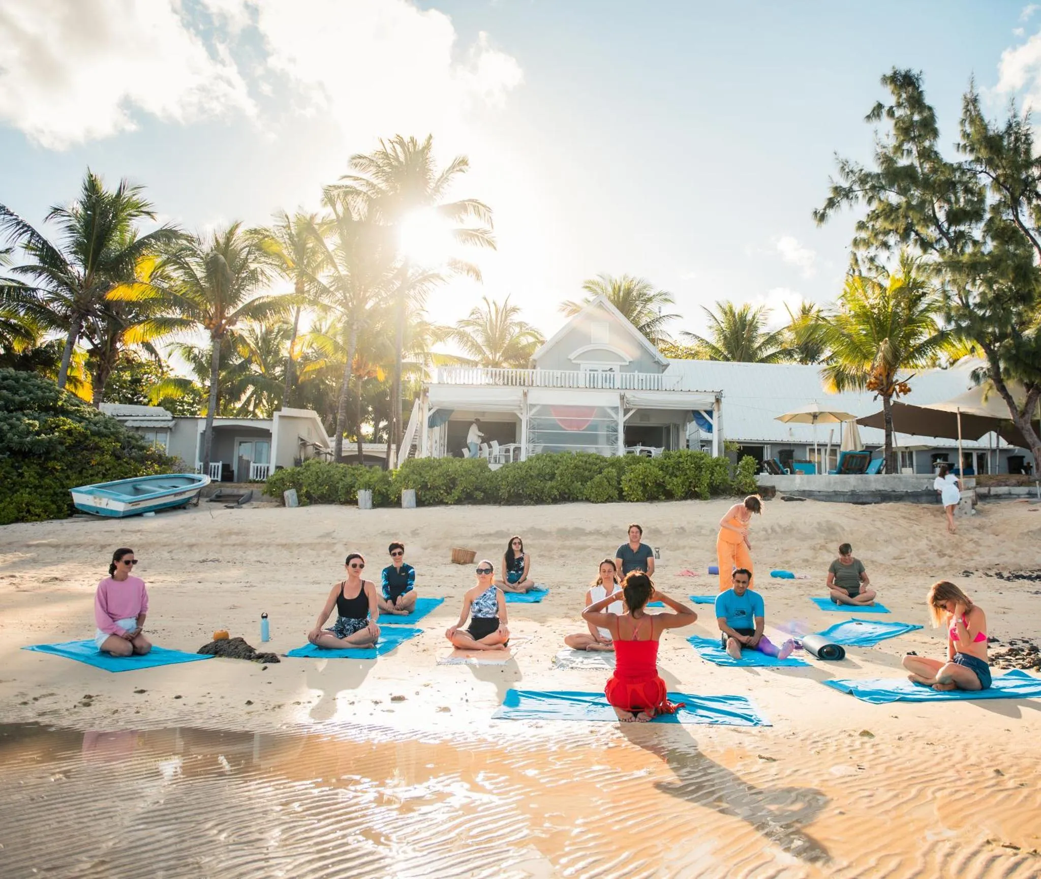 Personnes pratiquant le yoga sur une plage de sable blanc bordée de palmiers.