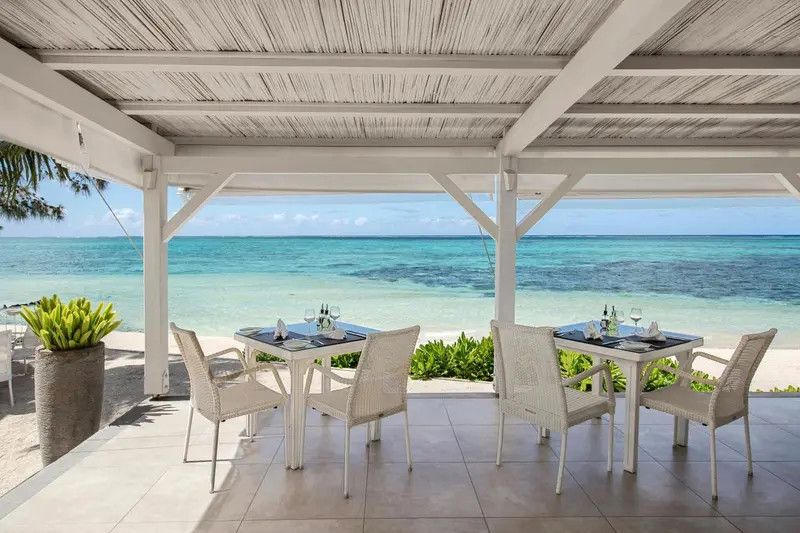 Tables de restaurant en plein air avec vue sur la mer turquoise.
