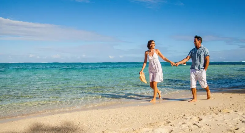 Un couple se promène main dans la main sur une plage de sable fin.