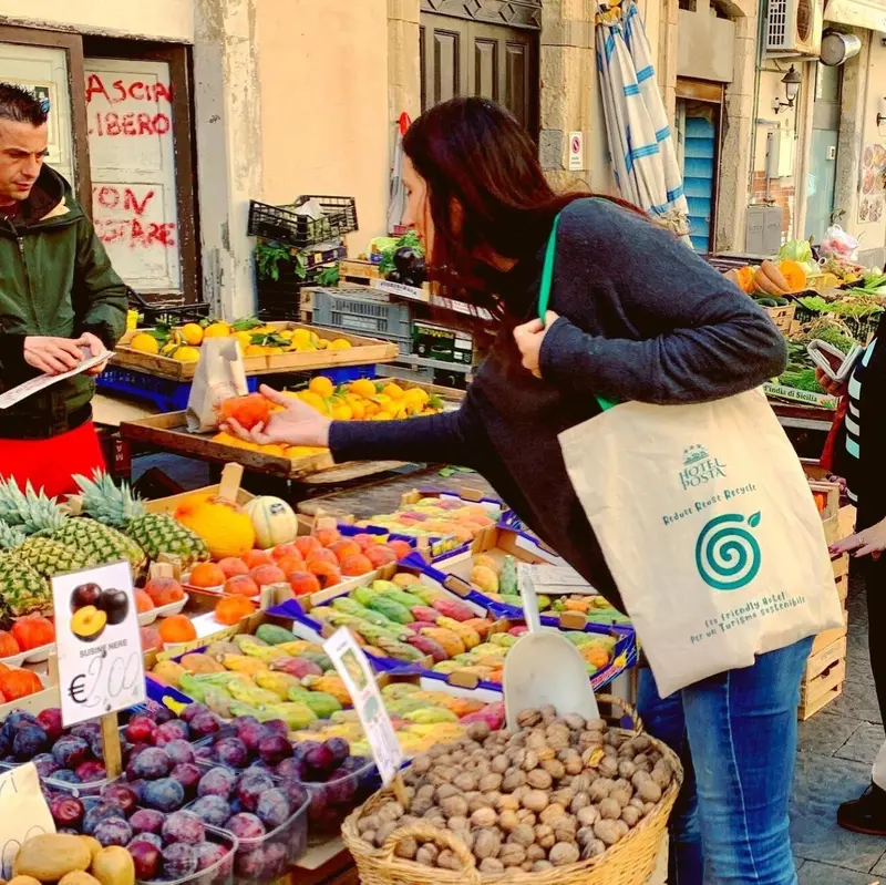 Une vendeuse présente des fruits et légumes à une cliente sur un marché ensoleillé.